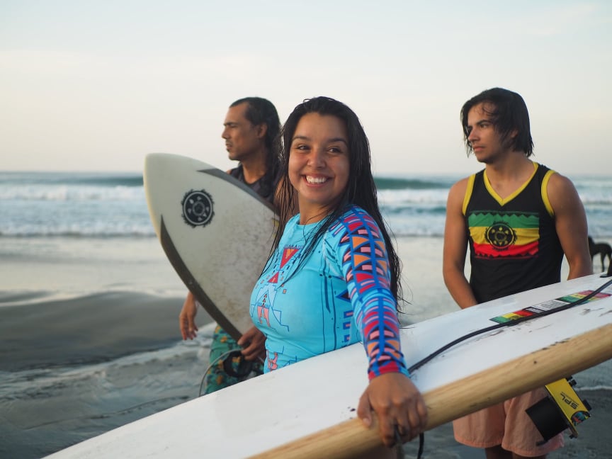 A group of teens carry surfboards on a beach